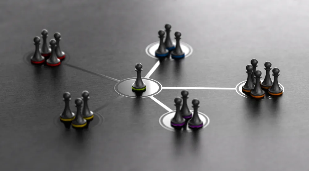 Concetto di segmentazione del pubblico o diversificazione della clientela rappresentato con pedine colorate su una superficie scura. Un gruppo principale di pedine è suddiviso in gruppi più piccoli, illustrando strategie di marketing, targetizzazione del pubblico e personalizzazione dei servizi.