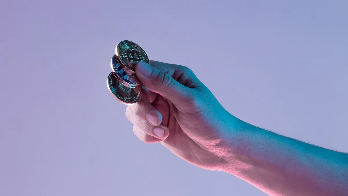 Una mano maschile che tiene i token delle principali criptovalute