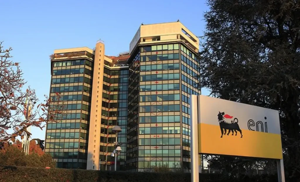Sede centrale di ENI con logo aziendale in primo piano e edificio moderno con vetrate riflettenti al tramonto.