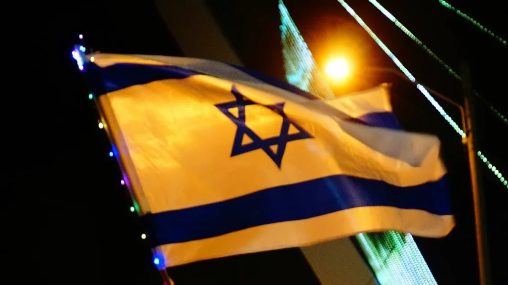 Persone camminano per strada di notte con la bandiera di Israele