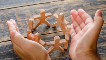 Due mani che proteggono degli omini di legno simboleggiano le attività sociali del Terzo Settore