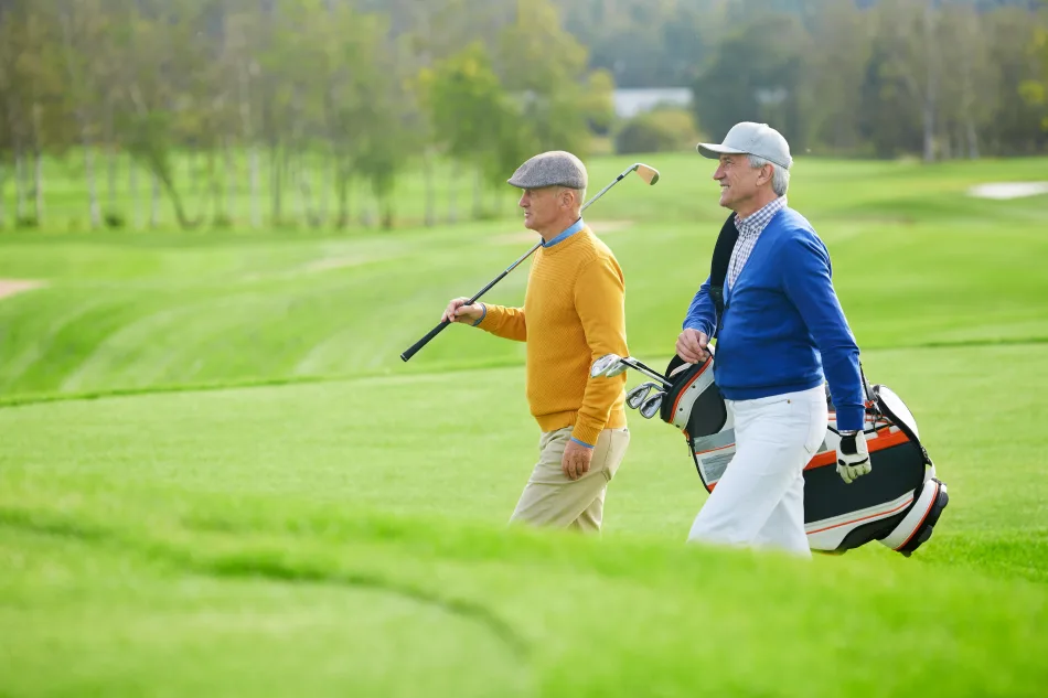 Due uomini senior che camminano su un campo da golf verde, indossando abbigliamento sportivo elegante e trasportando mazze da golf.