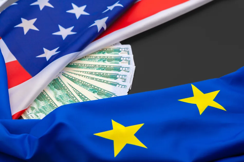 Banconote da 100 dollari tra le bandiere di Stati Uniti e Unione Europea