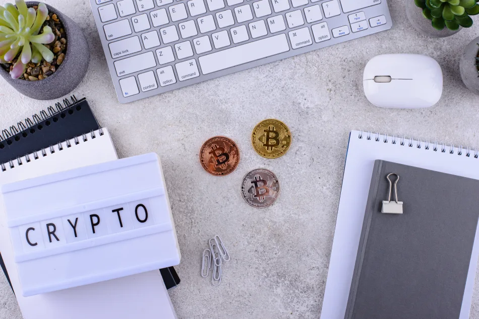 Scrivania con criptovalute, un'agenda, un pc e la scritta crypto su un foglietto di carta