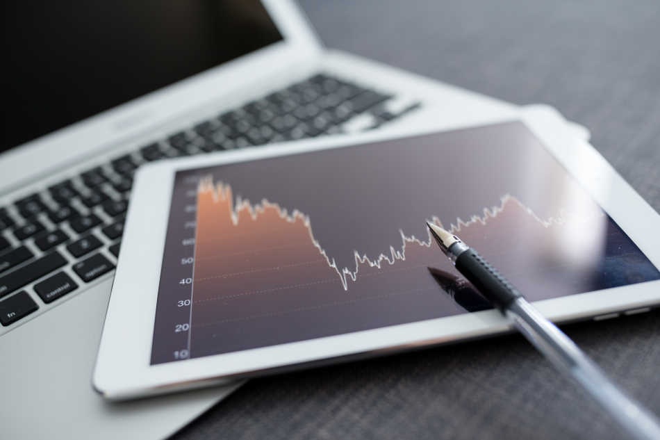 Un tablet, riportante un grafico lineare di un'attività finanziaria, poggiato sulla tastiera di un pc