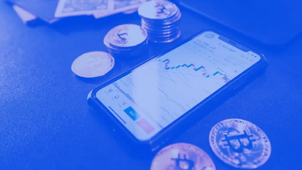 Uno smartphone con l'app di Bit2Me circondato da token di criptovalute