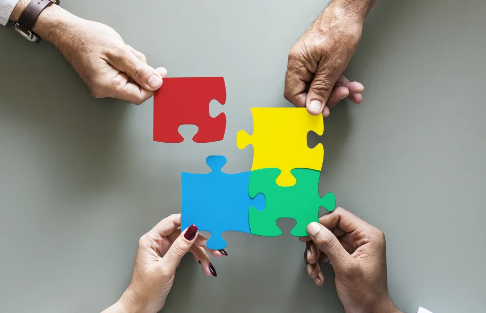 Quattro mani si uniscono al centro componendo le varie tessere di un puzzle colorato