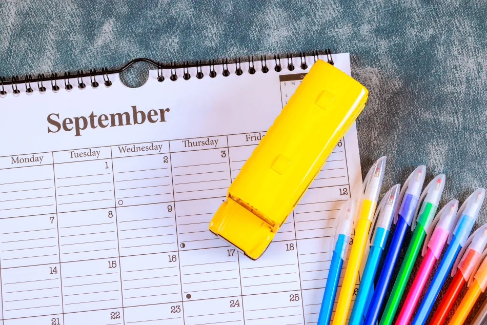 Su una scrivania sono poggiati un calendario del mese di settembre, un evidenziatore giallo e pennarelli di vari colori