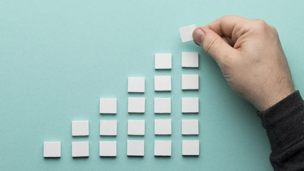 Una mano aggiunge tasselli ad una piramide di carta, rappresentazione grafica del processo di crescita di una startup