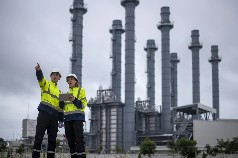 Due ingegneri davanti a un impianto industriale con numerose ciminiere