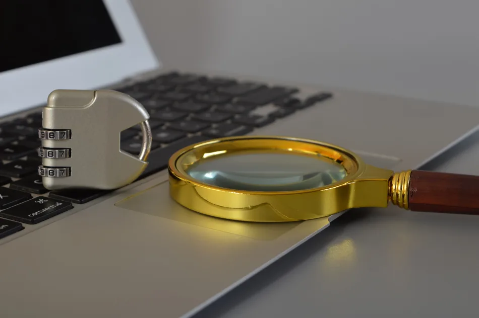 Una lente di ingrandimento e un lucchetto a codice chiuso, sono poggiati sulla tastiera di un laptop computer
