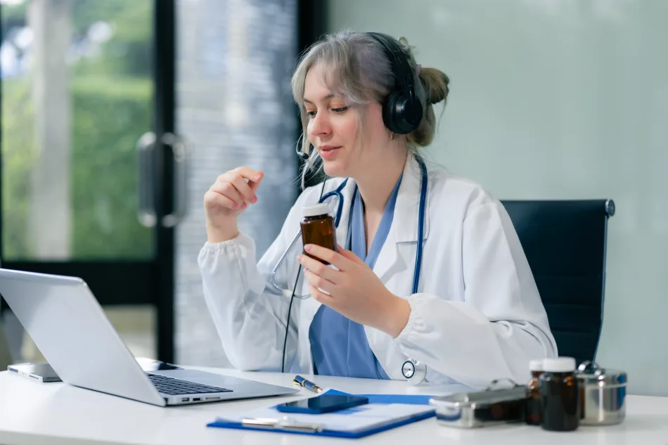 Telemedicina: una dottoressa in camice alla sua scrivania mostra a un paziente le medicine da prendere