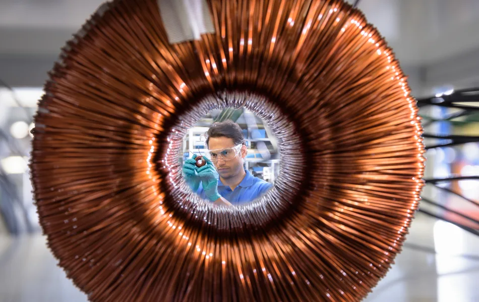 Un grande elettromagnete a forma di ciambella e un lavoratore che lo ispeziona