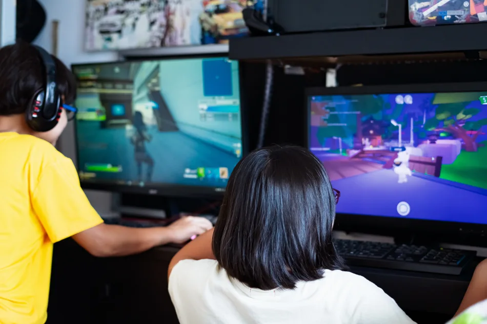 Ina coppia di giovani, davanti a due schermi, giocano ai videogames