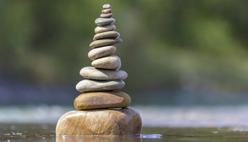 Sulla riva di un fiume, leggermente bagnati dalla corrente, una pila di sassi in equilibrio dal più grande, alla base, al più piccolo, in cima