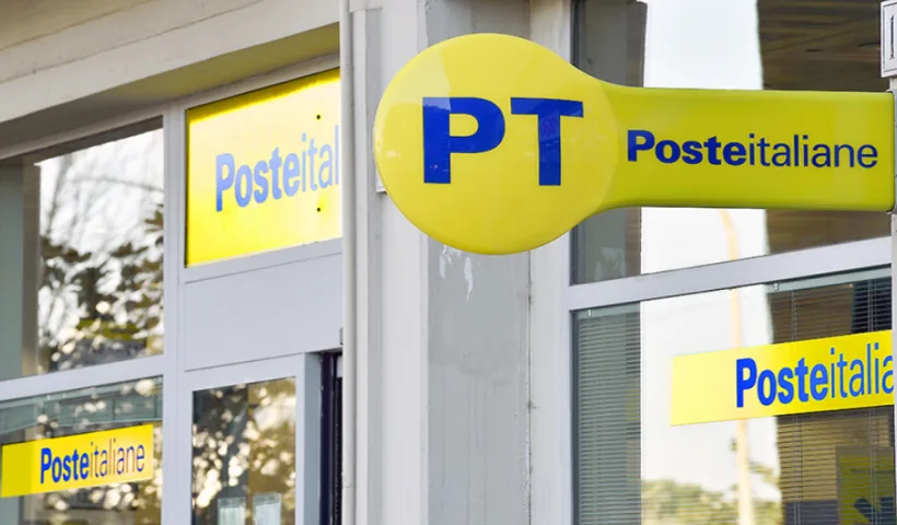 L'esterno di un ufficio postale. Sono visibili diversi cartelli sulle vetrine e il classico pannello circolare con le lettere PT di Poste Italiane