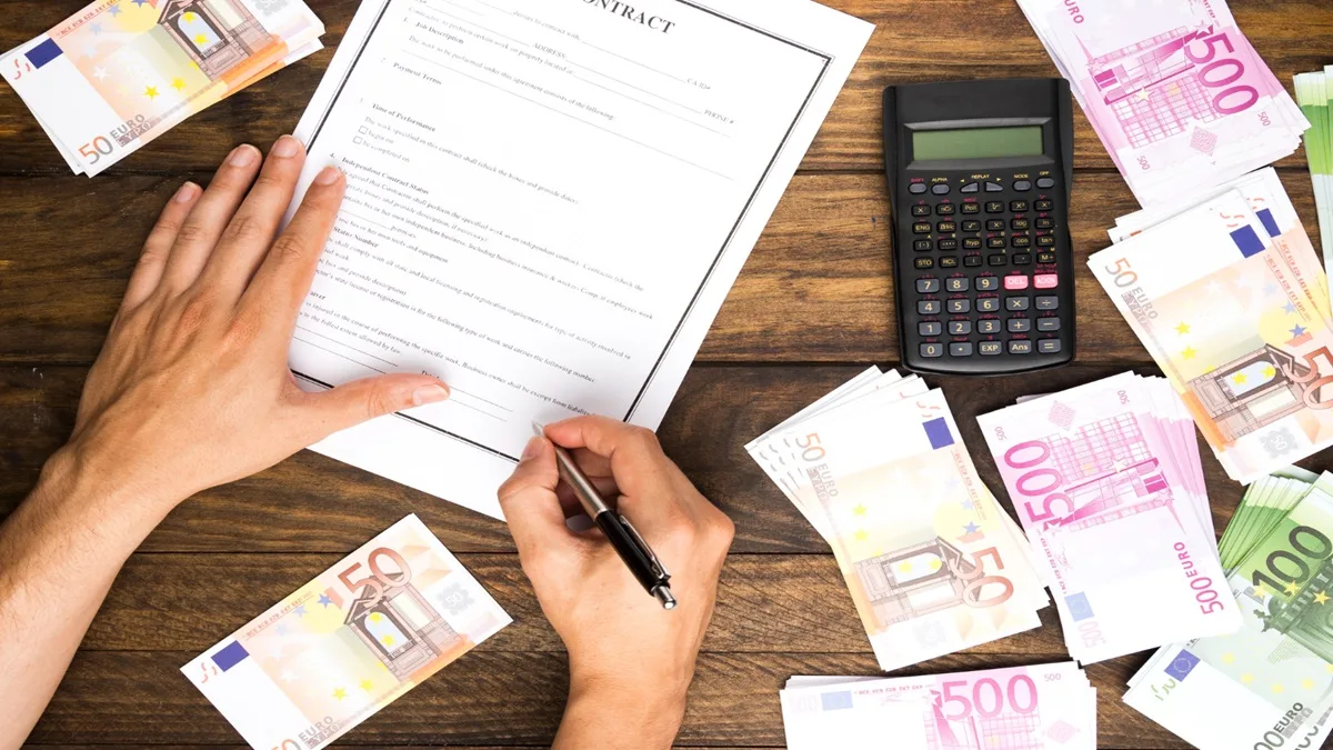persona che firma un documento tipo assegno di inclusione con banconote ed una calcolatrice sul tavolo