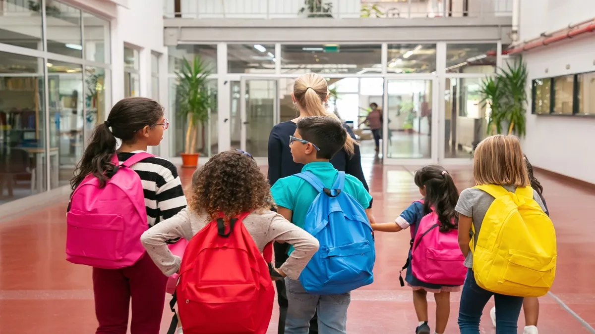 Gruppo di bambini con zaini colorati che entra a scuola con un’insegnante. immagine ideale per articoli sul Bonus Scuole Paritarie 2026.