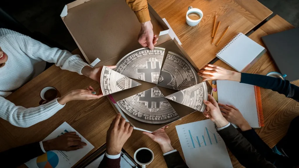 Persone attorno a un tavolo che dividono una moneta di Bitcoin in sezioni, simbolo della tassazione e della regolamentazione delle criptovalute nel 2026.