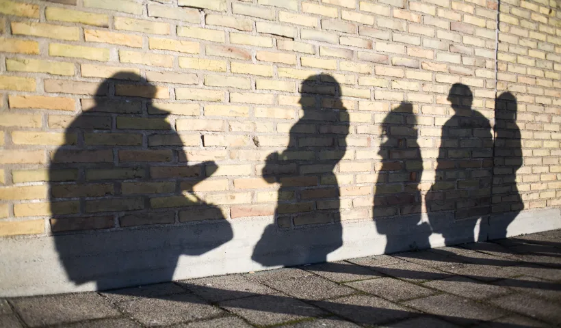 Le ombre nitide di alcune persone vengono proiettate su un muro di mattoni a indicare il concetto di economia ombra