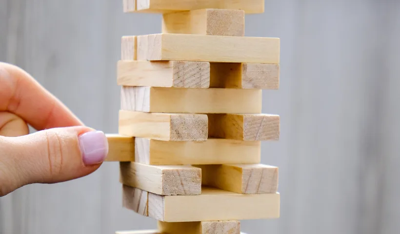 Gioco del Jenga. Una mano estrae un pezzetto di legno dalla torre, stando attenta a non farla cadere.