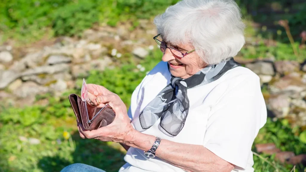 Donna anziana sorride mentre conta denaro dal portafoglio, simbolo degli aumenti delle pensioni di reversibilità 2026