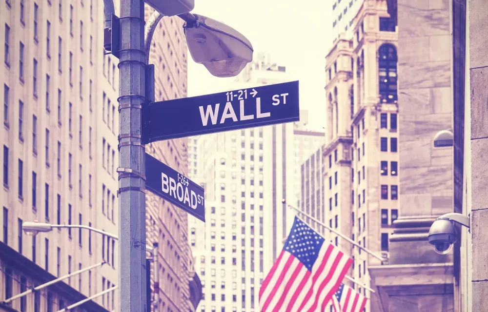 I cartelli stradali all'angolo tra Wall Street e Broad Street. Sullo sfondo le bandiere americane sui pennoni che pendono dalla Borsa Usa