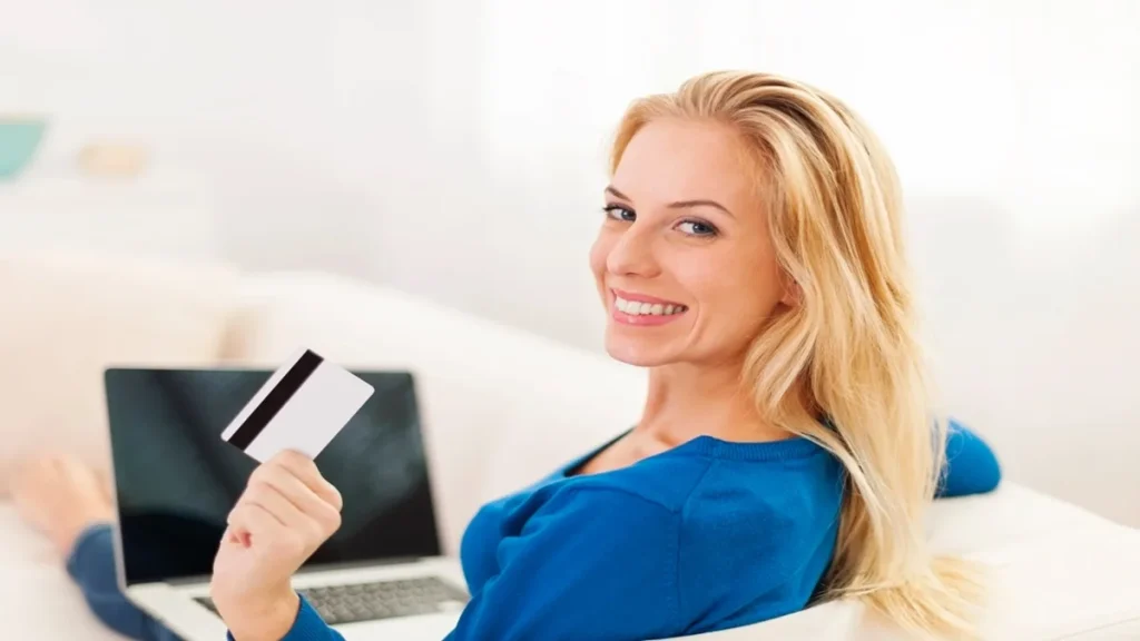 Donna sorridente con carta di credito in mano mentre usa il computer per gestire il conto corrente online