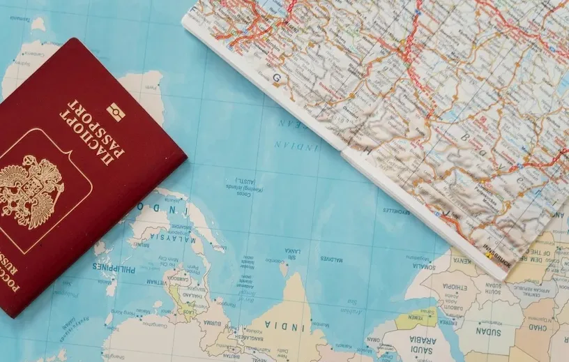 Passaporto rosso appoggiato su una mappa geografica con cartina stradale aperta accanto.