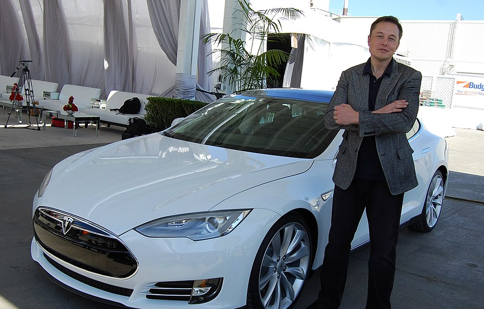 Elon Musk in piedi vicino a una Tesla bianca nel 2021