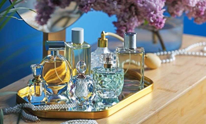 Boccette di profumo eleganti e con forme varie, alcune piene, altre vuote, sono poggiate su un vassoio dorato.