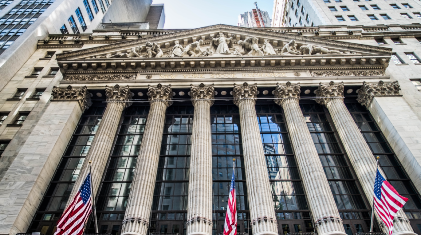 La facciata di Wall Street vista dal basso verso l'alto dalla base del palazzo. Tre bandiere degli Stati Uniti pendono su tre pennoni