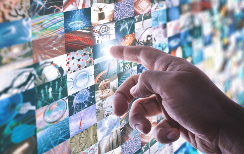 Una mano indica uno schermo al cui interno sono riportate tante fotografie a tema tecnologia e ricerca