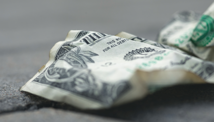 Un dollaro stropicciato giace su un pavimento color grigio