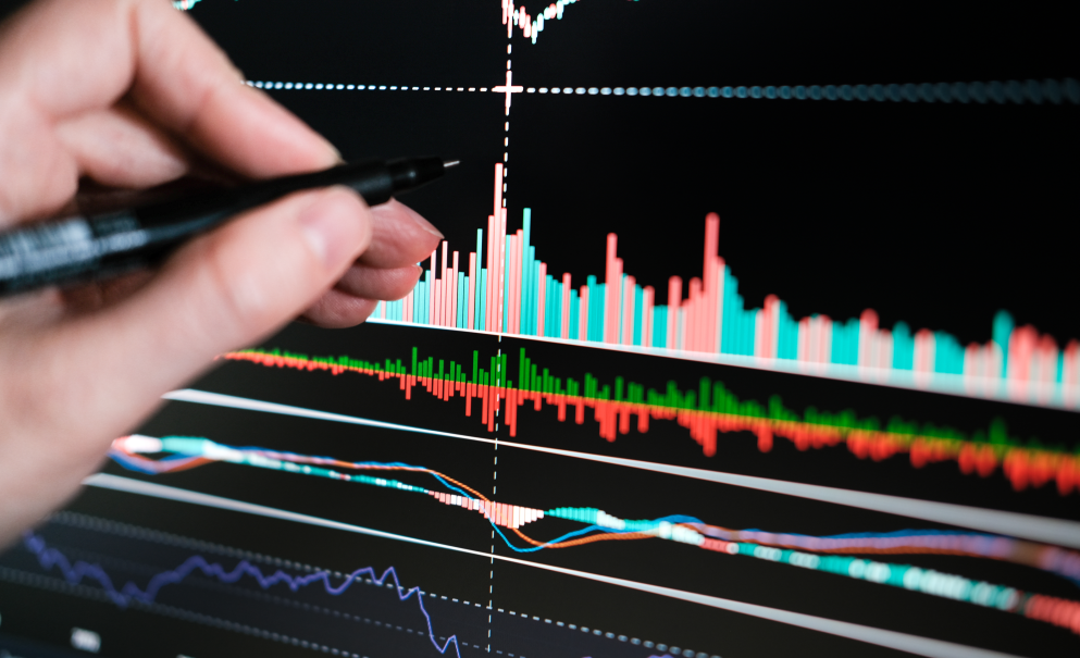 Una mano con una penna indica uno schermo di pc con un grafico di Borsa a candele