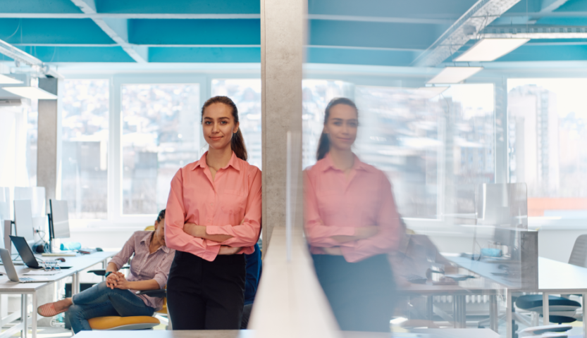 Una donna, in un ampio ed elegante ufficio, poggiata a una parete che la riflette. Una dirigente