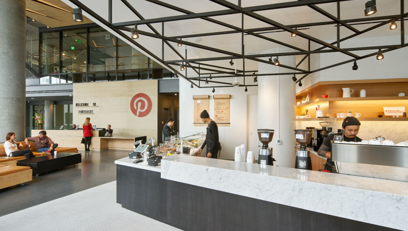 La hall di ingresso della sede di Pinterest. Sullo sfondo il dex, con il logo della società, in primo piano un caffè aziendale. Alcune persone sono sedute su dei divanetti