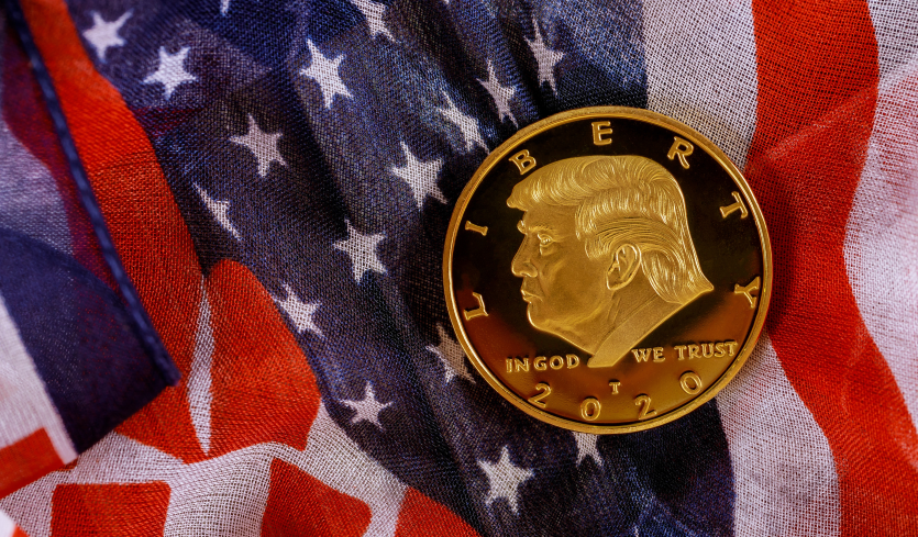 Una moneta d'oro con il profilo di Donald Trump, poggiata su una bandiera Usa