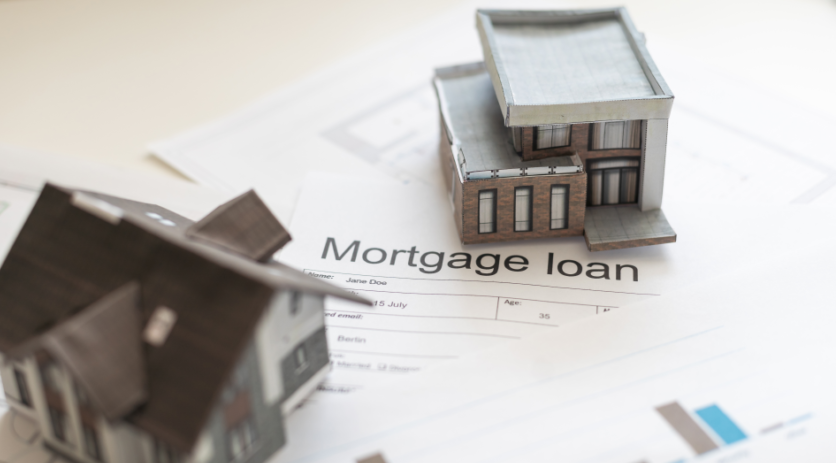 Dei modellini di abitazioni sono poggiati su alcuni fogli che riportano grafici sull'andamento dei mercati immobiliari