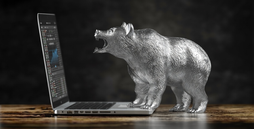 Una statuetta d'argento a forma di orso ruglia contro uno smartphone che riporta alcune quotazioni di Borsa