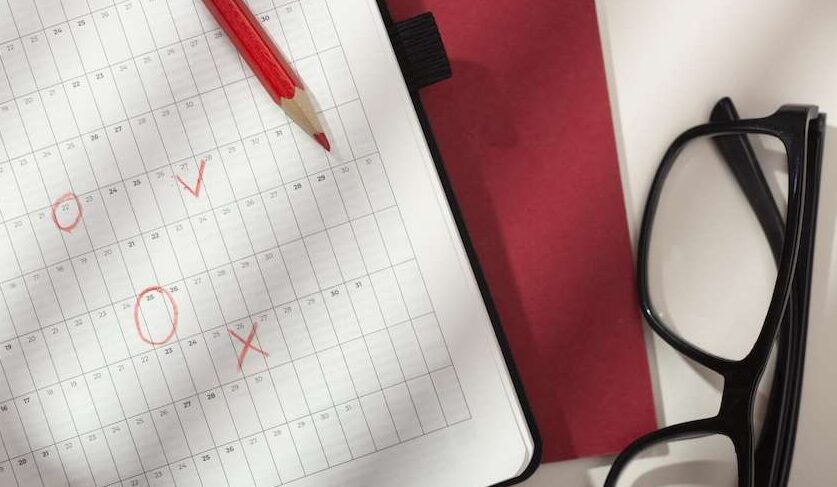 Calendario con date cerchiate e penna rossa per scadenze fiscali marzo 2026 su scrivania con occhiali.