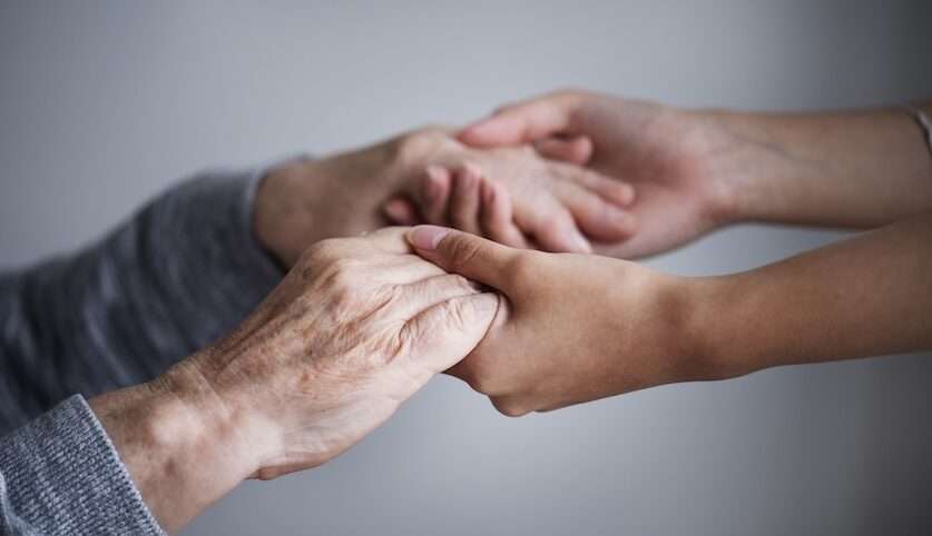 Mani di una persona anziana e di un volontario che si stringono, simbolo di partecipazione e servizio civile over 65