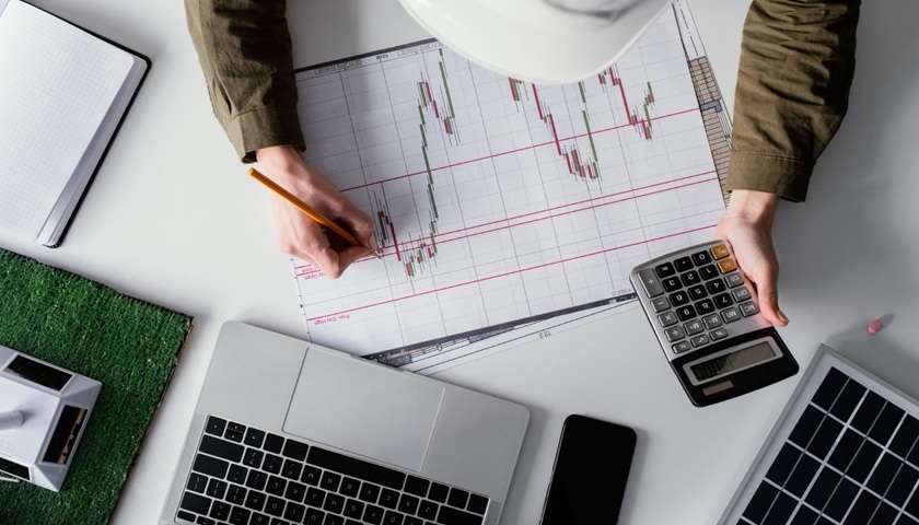 Scrivania con grafico finanziario, calcolatrice e computer portatile mentre una persona analizza l’andamento dei mercati. L’immagine rappresenta il BTP Valore 2026, le possibili variazioni dei tassi di interesse e le valutazioni da fare prima di investire nella nuova emissione.