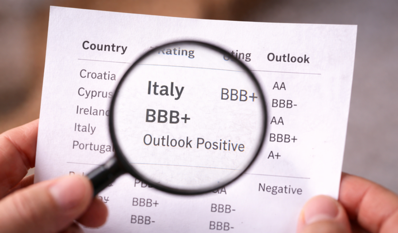 Documento con rating sovrano dell’Italia osservato attraverso una lente d’ingrandimento, simbolo dell’attenzione dei mercati sul profilo di credito del Paese.