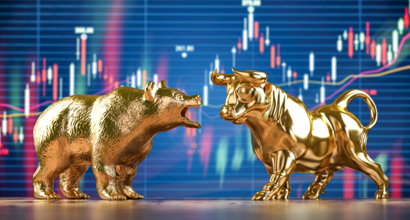 Due statuette d'oro, un orso e un toro, posizionate davanti a uno schermo che mostra un grafico a candele