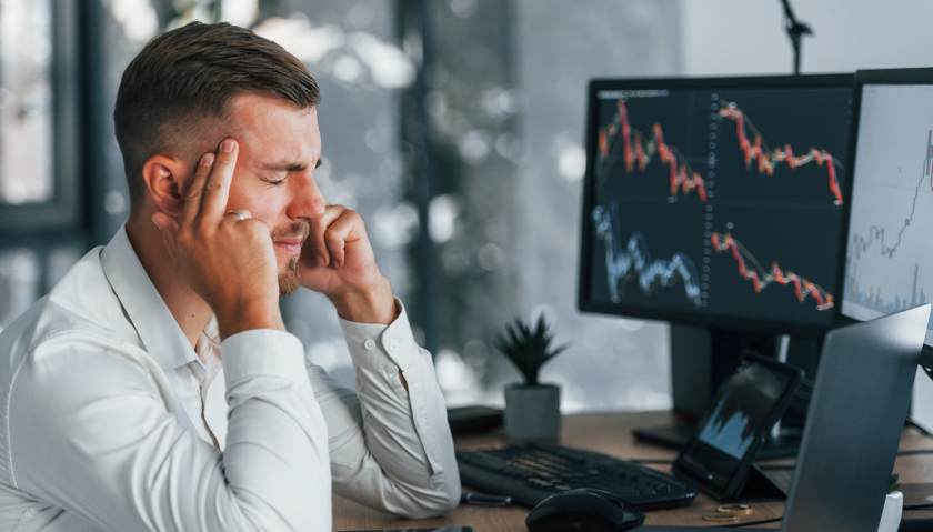 Un trader preoccupato davanti a schermi con grafici azionari