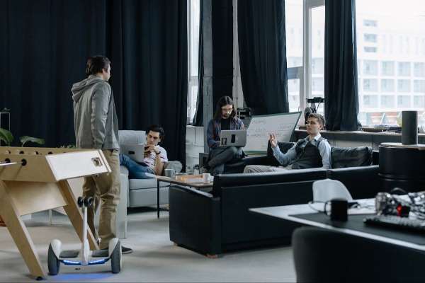 Giovani professionisti in un ambiente di lavoro moderno e informale con laptop, hoverboard e tavolo da calcetto