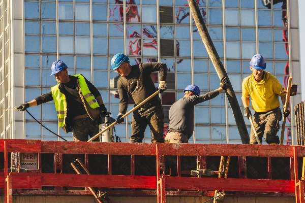 Operai edili con elmetti blu al lavoro su un cantiere con strutture metalliche ross
