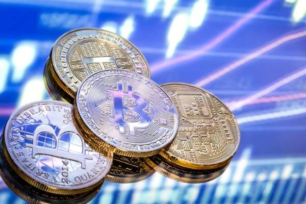 Monete fisiche raffiguranti criptovalute su sfondo con grafici finanziari, utilizzate per illustrare come dichiarare i crypto‑asset nel Modello 730/2026.