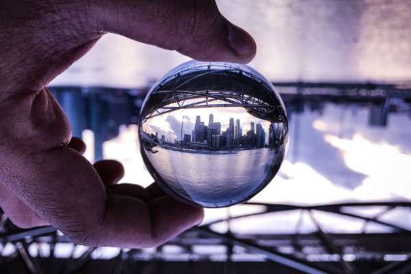 Una sfera di cristallo di ridotte dimensioni, tenuta tra le dita di una mano, riflette a fuoco una city bancaria sullo sfondo